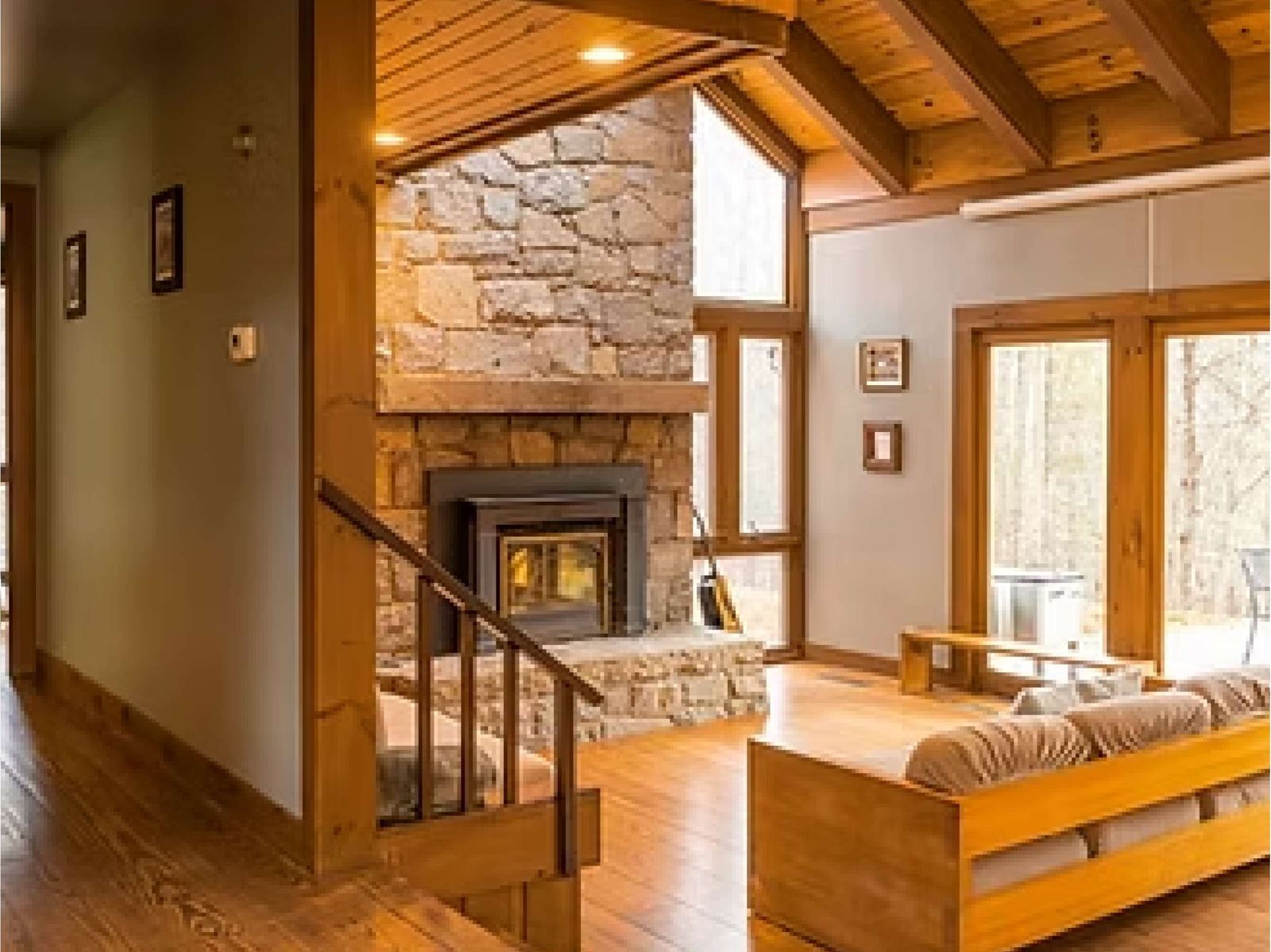 Living room with a stone fireplace, wood ceilings and tall windows